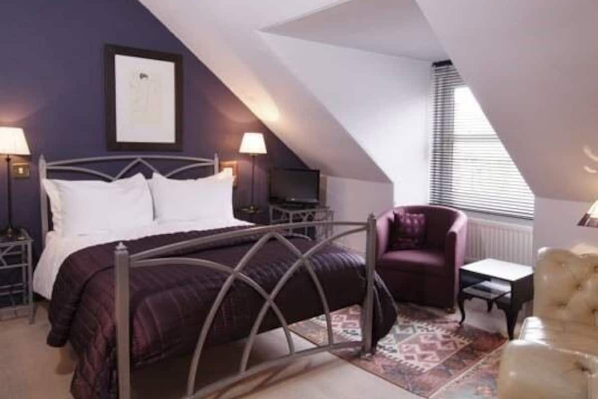A bedroom with a bed, a chair, a desk, and a radiator.