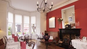 Een eetkamer met gedekte tafels, een open haard en een groot raam met gordijnen.