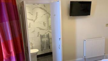 Une salle de bain d’hôtel équipée de toilettes, d’un porte-serviettes, d’un radiateur et d’un téléviseur fixé au mur.