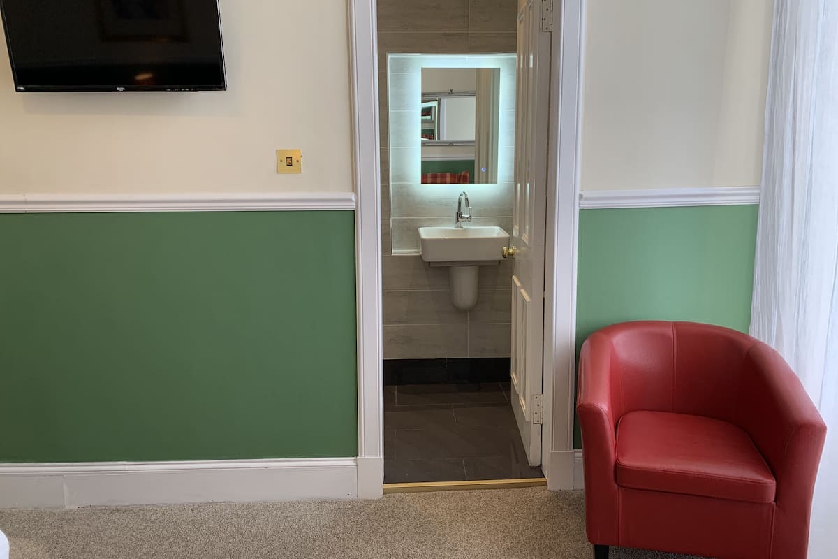 A room with green walls, a white door, a red chair, a TV mounted on the wall, and a bathroom visible through the door.