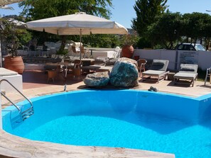 A swimming pool with lounge chairs and umbrellas, surrounded by outdoor seating and potted plants. - Gorgona Studios (Rhodes)