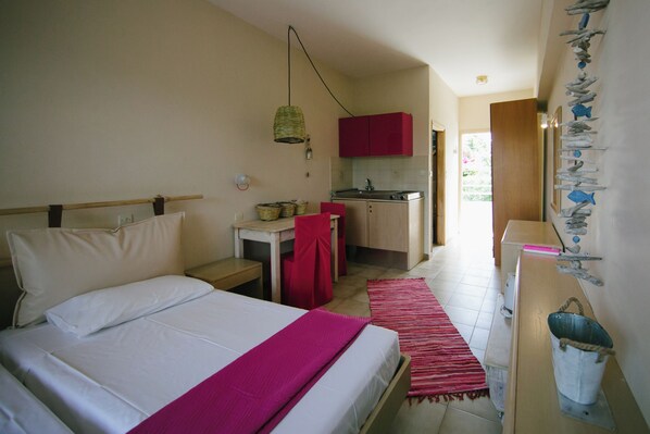 A bedroom with a bed, a desk, a kitchenette, and a bathroom.