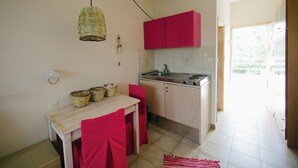 A compact kitchen with a wooden table, red chairs, a hanging light, and a red cabinet. - Gorgona Studios (Rhodes)