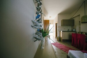 A room with a wooden bench, a wall-mounted plant, and a kitchen area in the background. - Gorgona Studios (Rhodes)