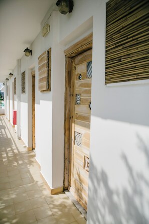 A corridor with wooden doors and windows, a tiled floor, and a wall with a number plaque. - Gorgona Studios (Rhodes)