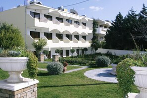 A multi-story hotel with a symmetrical facade, multiple balconies, and a well-maintained garden with various shrubs and a central pathway. - Gorgona Studios (Rhodes)