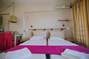 Ett dubbelrum med två sängar, ett skrivbord, en stol, en hänglampa och en luftkonditioneringsanläggning.