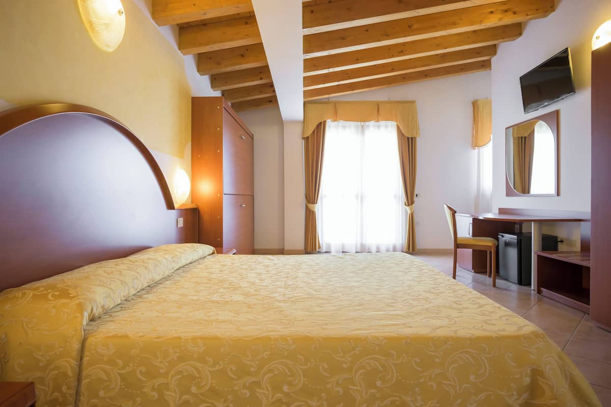 A bedroom with a large bed, a desk, a chair, a television, and a mirror.
