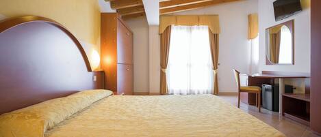A bedroom with a large bed, a desk, a chair, a television, and a mirror.