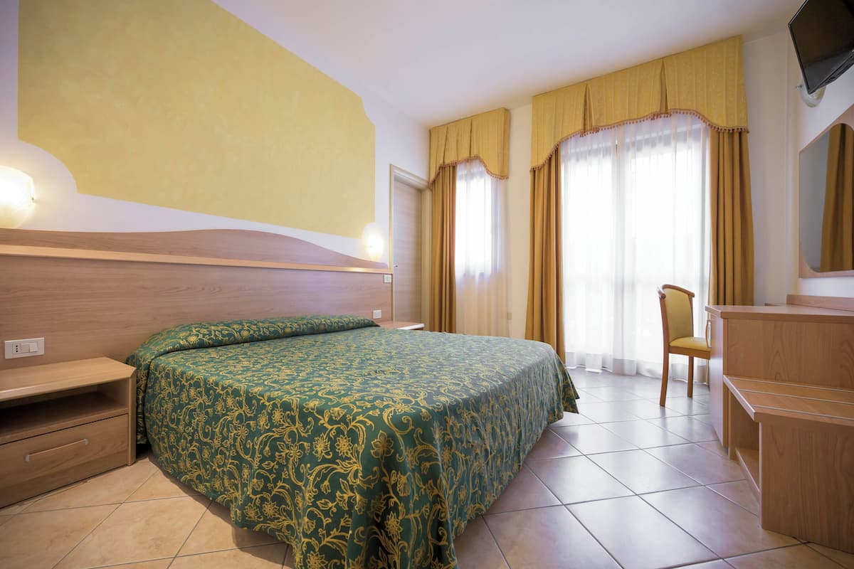 A hotel room with a bed, a desk, a chair, and a television.