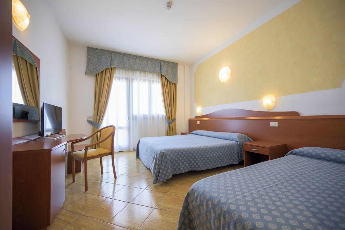 A hotel room with two beds, a desk, a chair, and a television.