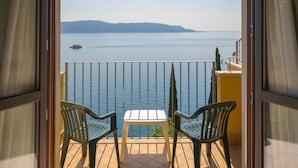 Een balkon met uitzicht op een rustige zee en verre heuvels. Er staan twee stoelen en een klein tafeltje.