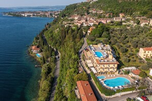 An aerial view of a coastal hotel with a swimming pool, surrounded by lush greenery and a clear view of the sea. - Hotel Piccolo Paradiso (Toscolano Maderno)