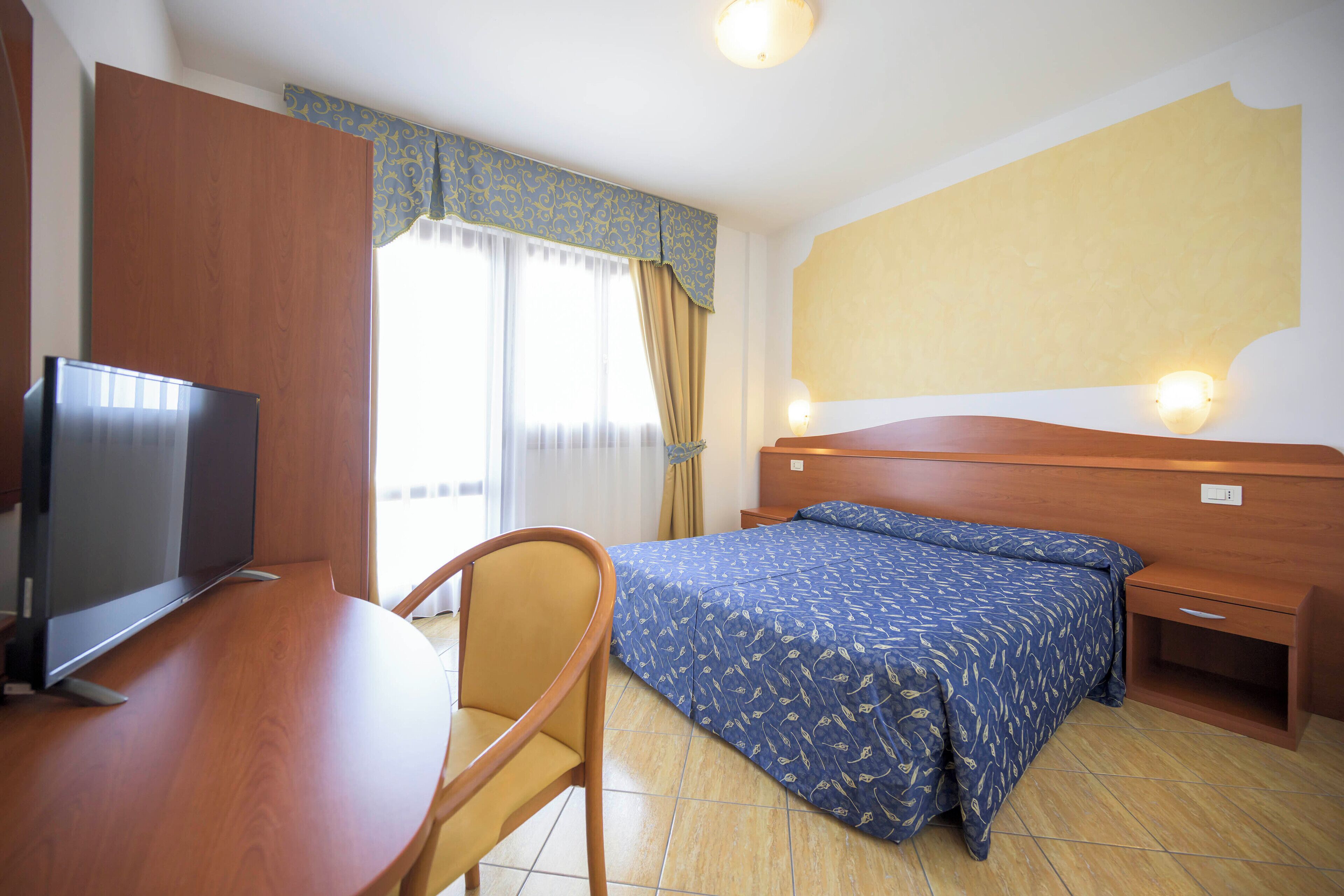 Una habitación de hotel con cama, televisión, escritorio y silla.