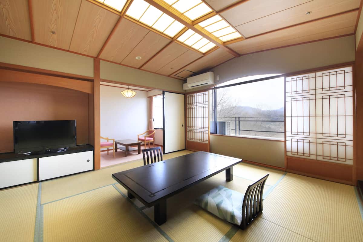 Um quarto japonês tradicional com tatames, uma mesa baixa, uma televisão e portas de correr.