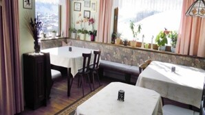 A cozy dining area with tables and chairs, a bench, and a view of a snowy landscape through the window. - Pension Niedermuhlbichler (Soell)