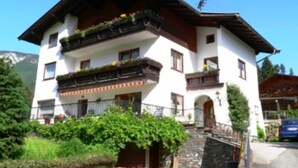 A two-story building with balconies, a stone staircase, and a mountain backdrop. - Pension Niedermuhlbichler (Soell)