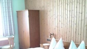 A double bed with white linens, a wooden wardrobe, a wooden headboard, and a small bedside table with a lamp. - Pension Niedermuhlbichler (Soell)