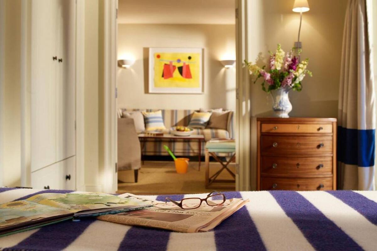 Quarto de hotel com cama, mesa de cabeceira, penteadeira, um vaso com flores e um quadro na parede.