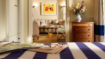 Habitación de hotel con cama, mesita de noche, cómoda, un florero con flores y un cuadro en la pared.