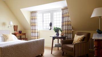 A bedroom with a bed, a chair, a small table, and a window with curtains.