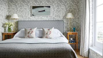 Une chambre à coucher bien rangée, avec un grand lit, deux tables de chevet avec des lampes, un tableau encadré au mur et une fenêtre avec des rideaux.