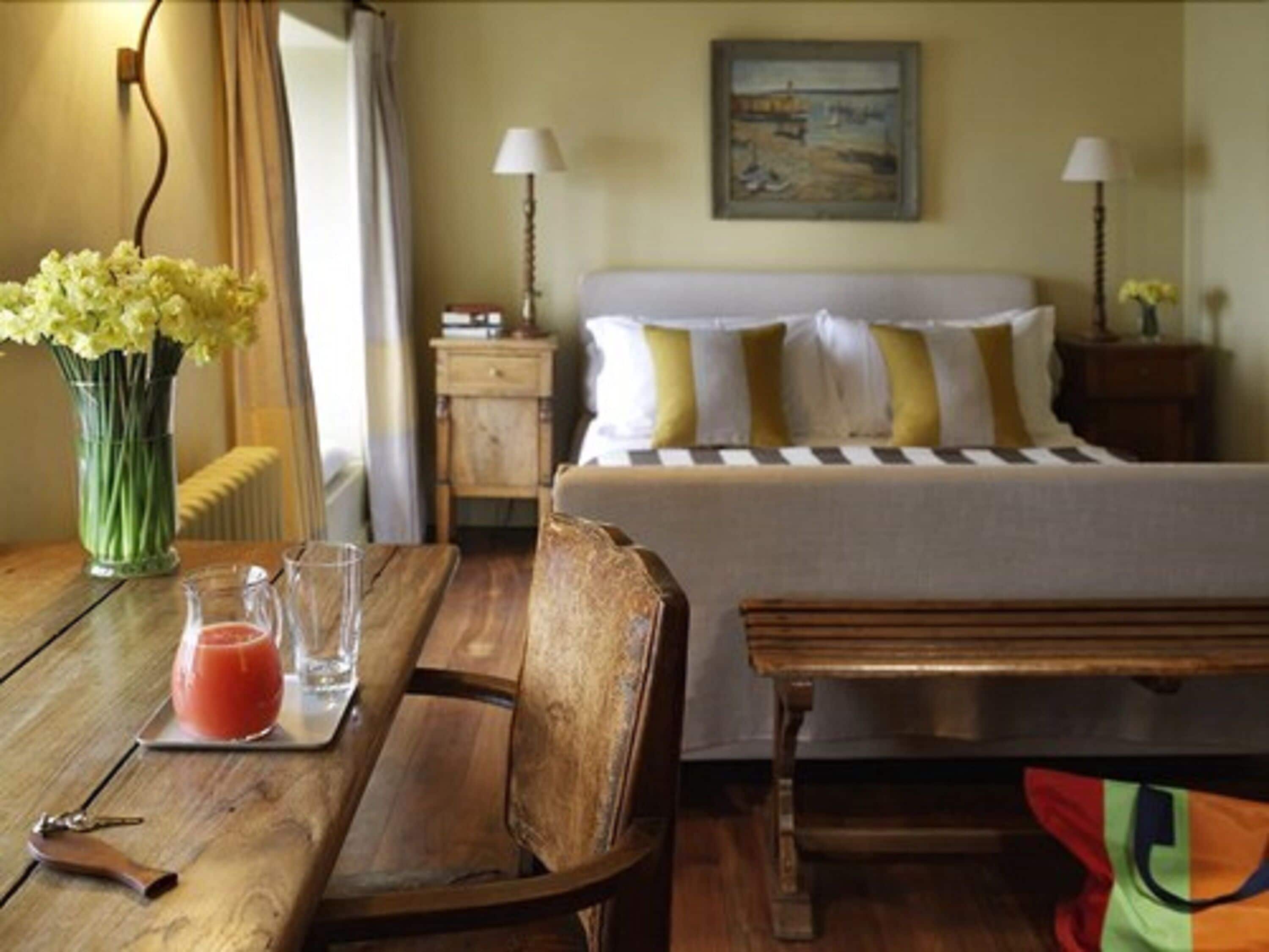 A hotel room with a bed, bedside tables, a wooden table with a drink and keys, and a bench.