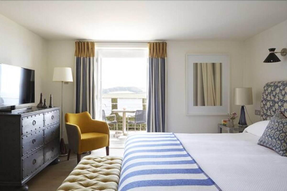 Quarto de hotel com cama, penteadeira, cadeira, abajur e vista para o exterior.