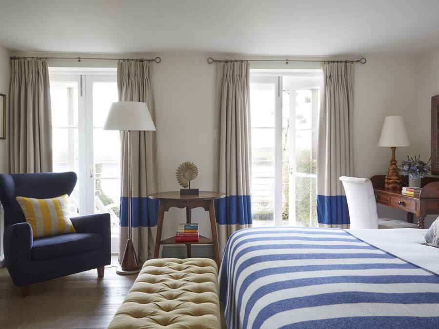 A hotel room with a bed, a chair, a table with a lamp, and a desk with a lamp.