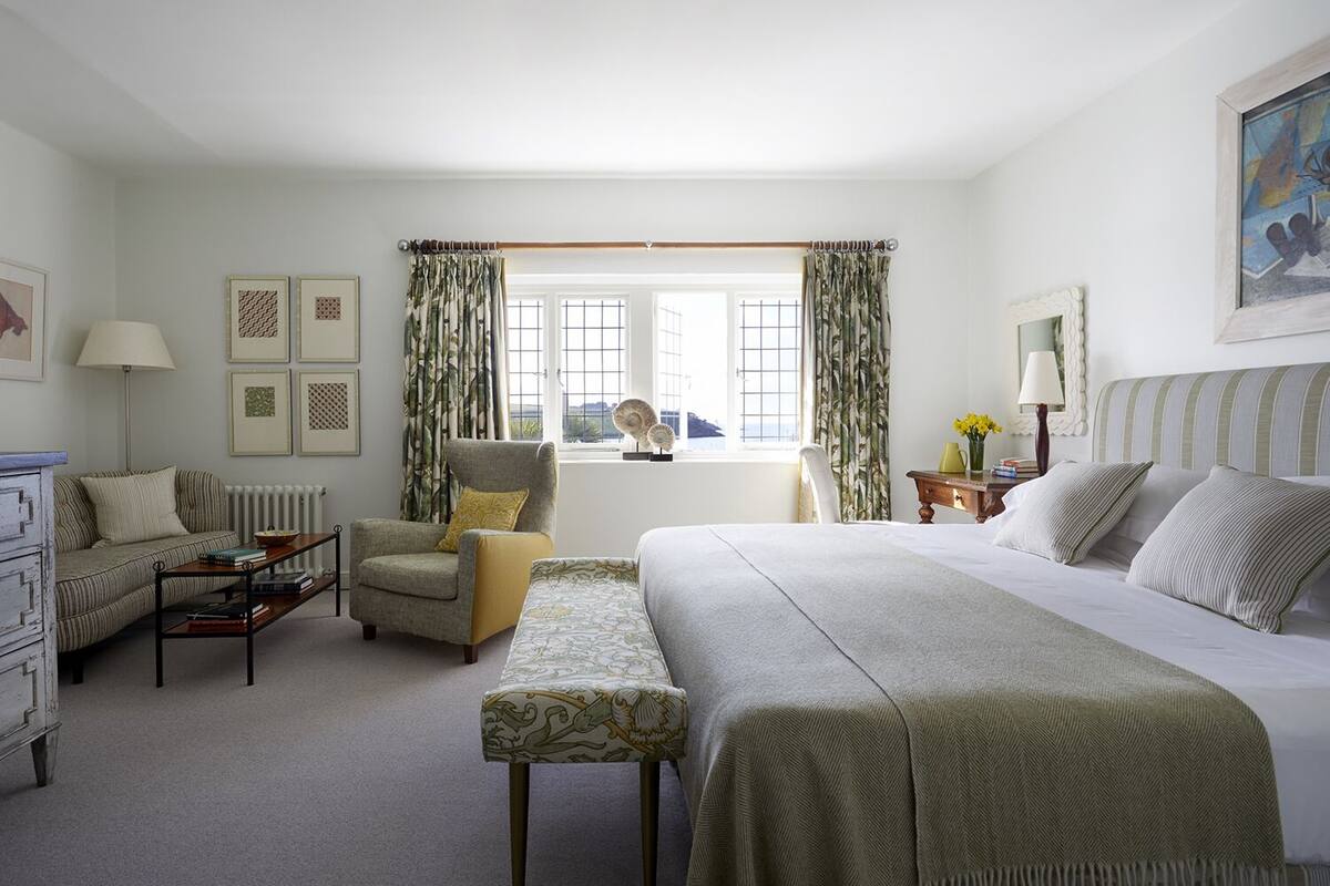 Quarto de hotel com uma cama, uma cadeira, uma escrivaninha e uma janela com cortinas.