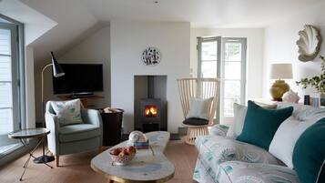 A cozy living room with a fireplace, a sofa, a chair, and a small table with a bowl of fruit.