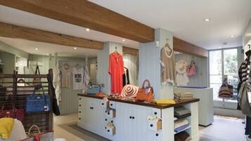 A boutique hotel interior with a central island displaying handbags and accessories, a wooden ceiling, and a view of the outdoors through large windows.