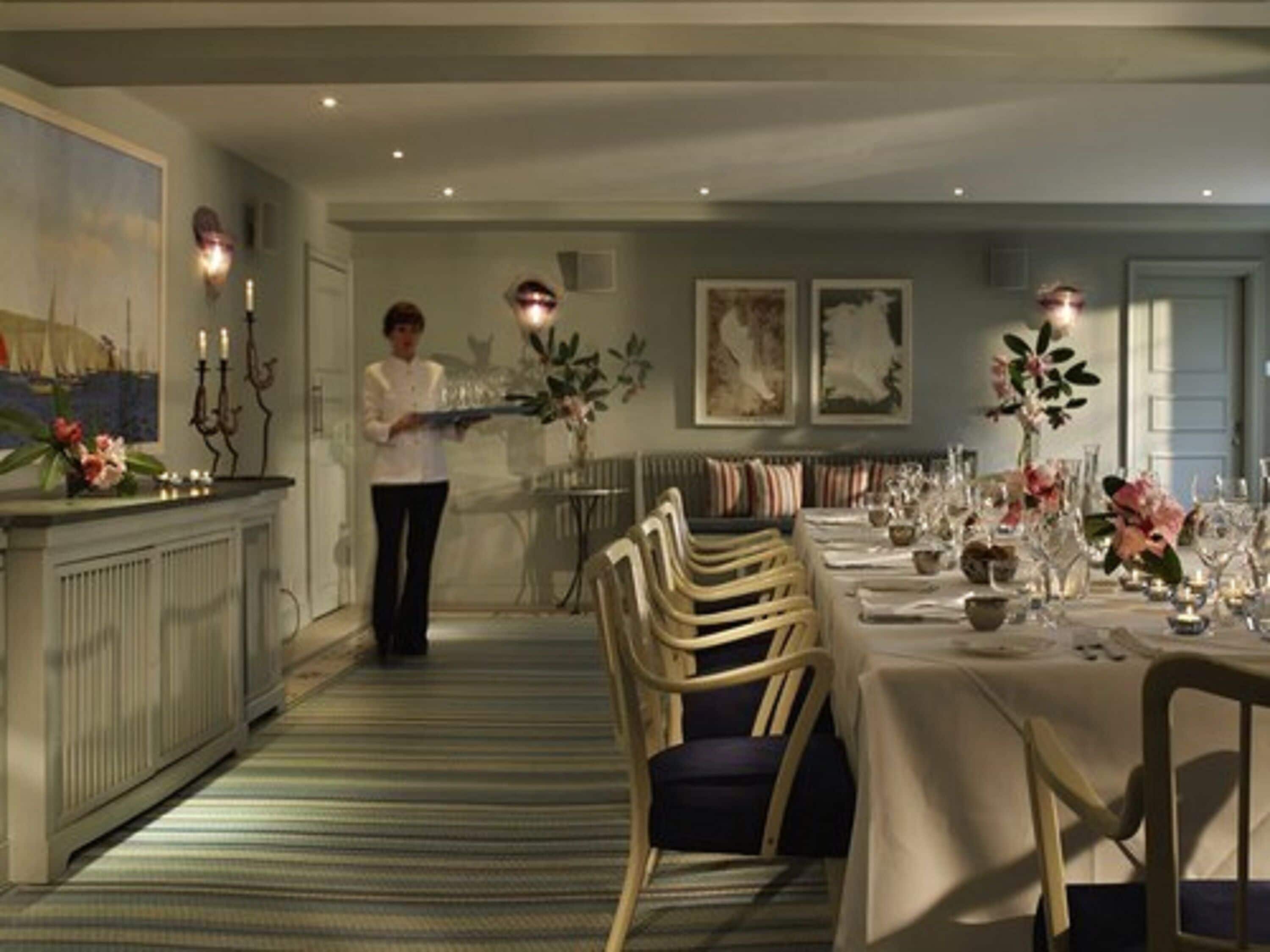 A dining area with a long table set for a meal, a bar area with a counter and candelabras, and a sofa in the background.