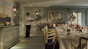 A dining area with a long table set for a meal, a bar area with a counter and candelabras, and a sofa in the background.