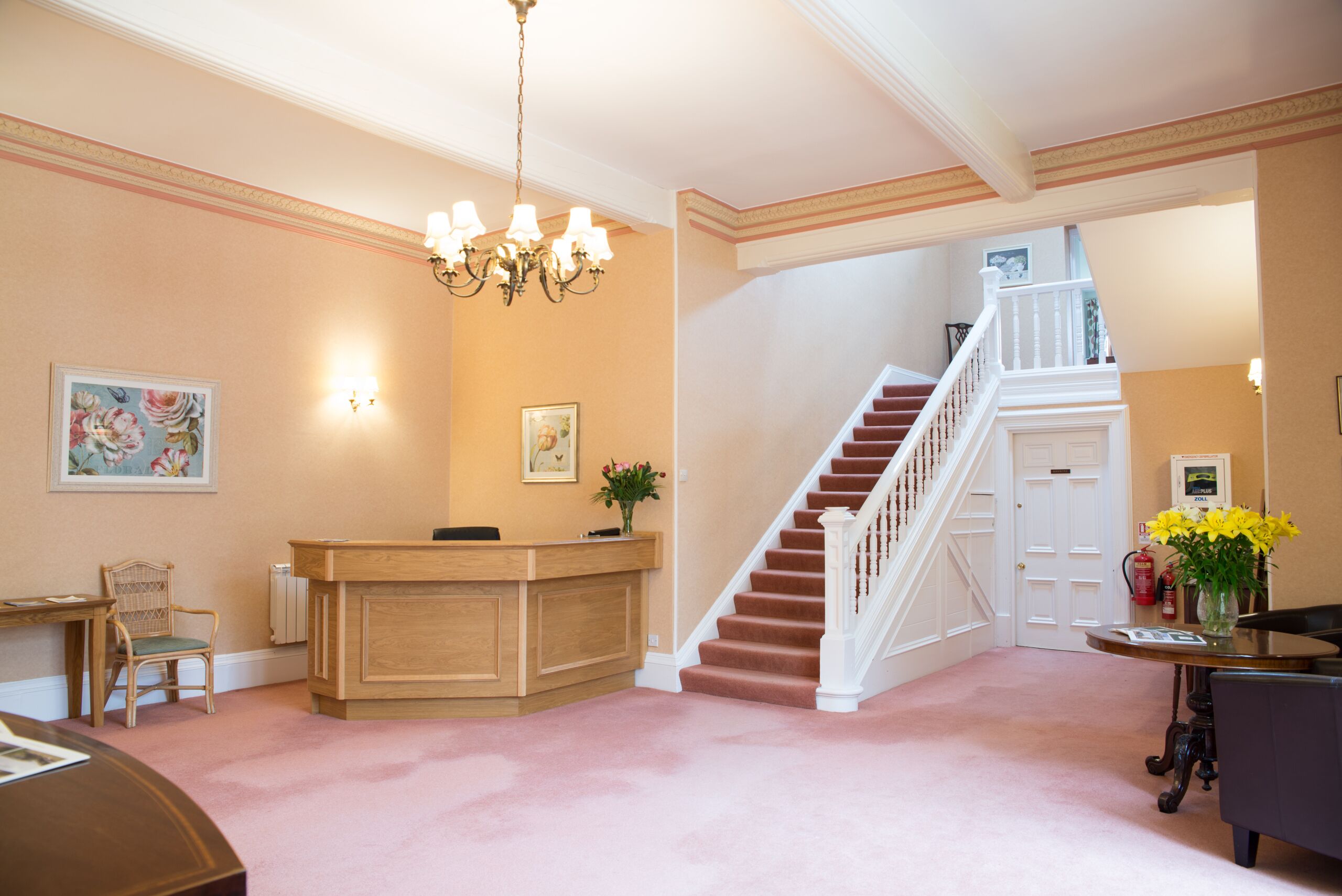 Un espace d’accueil comprenant un bureau en bois, une chaise, un escalier et un lustre.