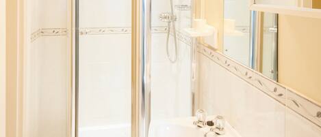 A bathroom with a glass-enclosed shower, a sink, and a mirror.