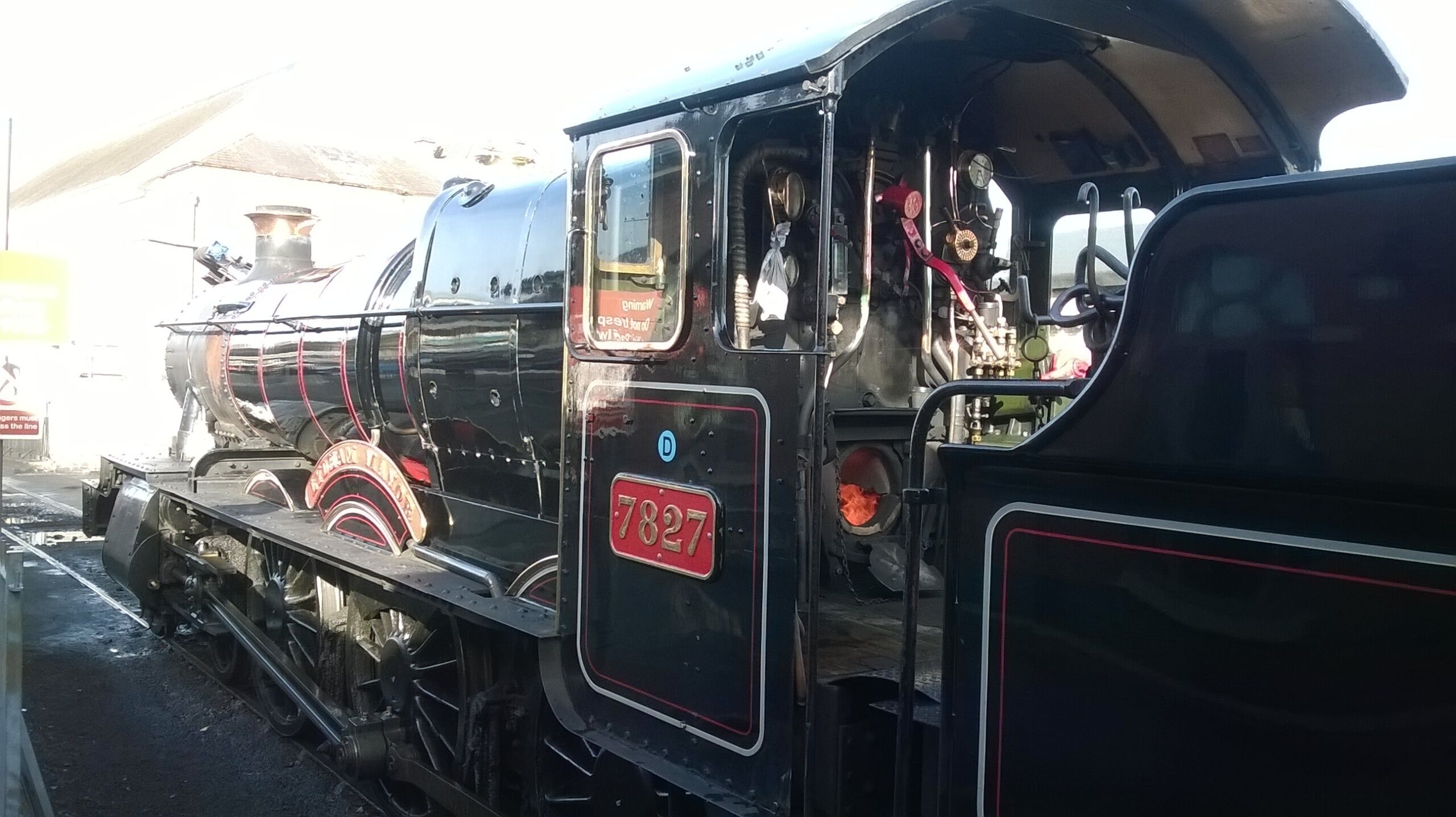 A vintage steam locomotive with visible mechanical components and a red "7827" plate.