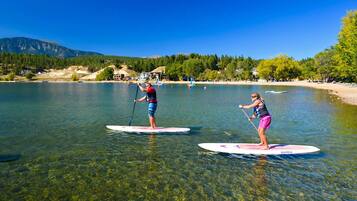 Dos personas haciendo paddleboard en un lago tranquilo con montañas al fondo.