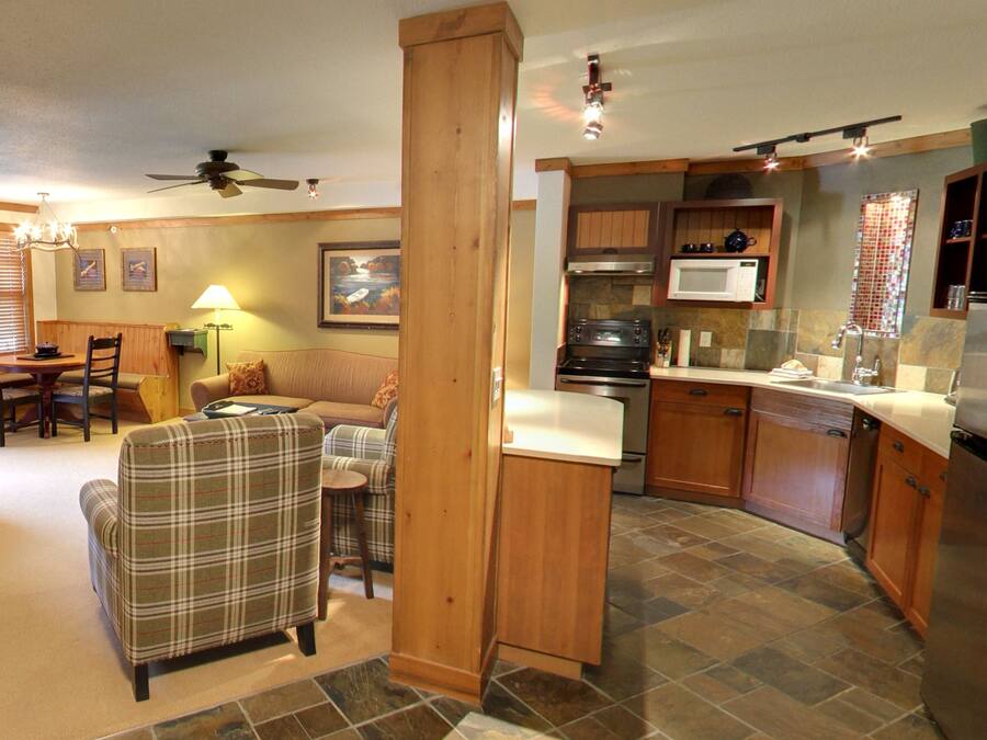 A kitchen with wooden cabinets, a microwave, and a refrigerator. There is a dining area with a table and chairs.