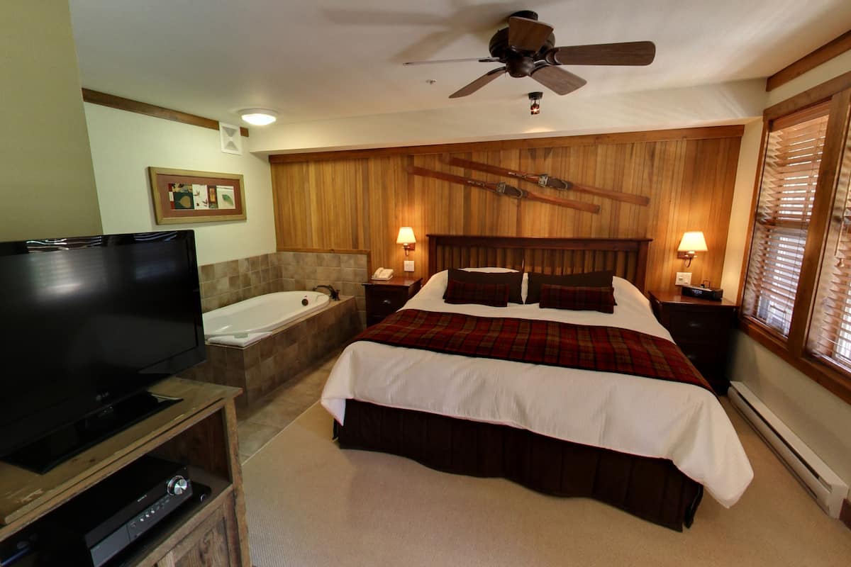 A bedroom with a large flat-screen TV, a wooden headboard, a bathtub, and two bedside lamps.