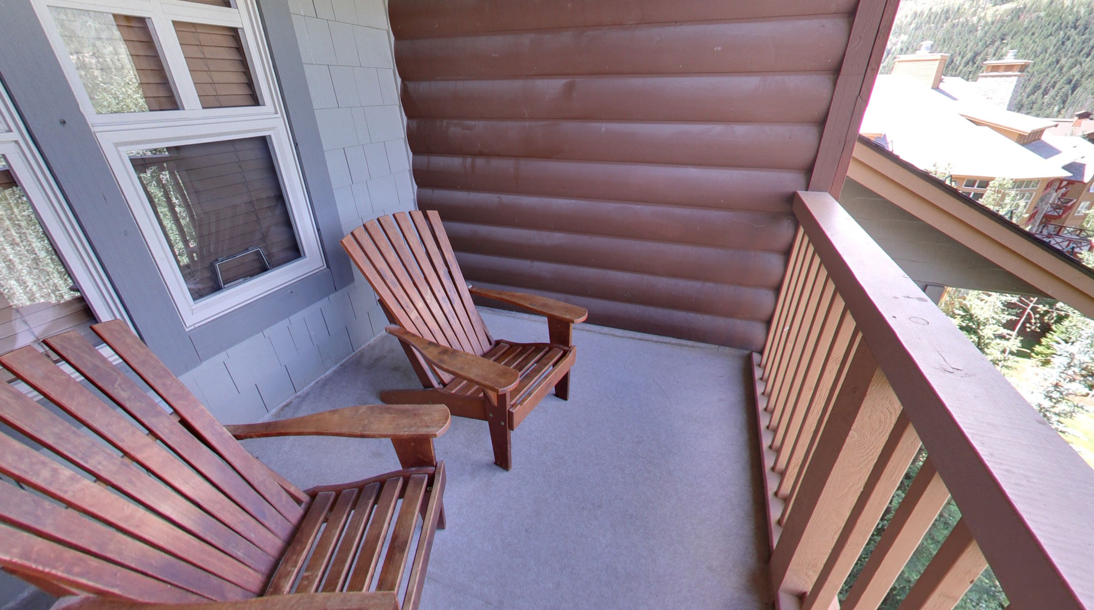 Una terraza de madera con dos sillas Adirondack y una ventana.