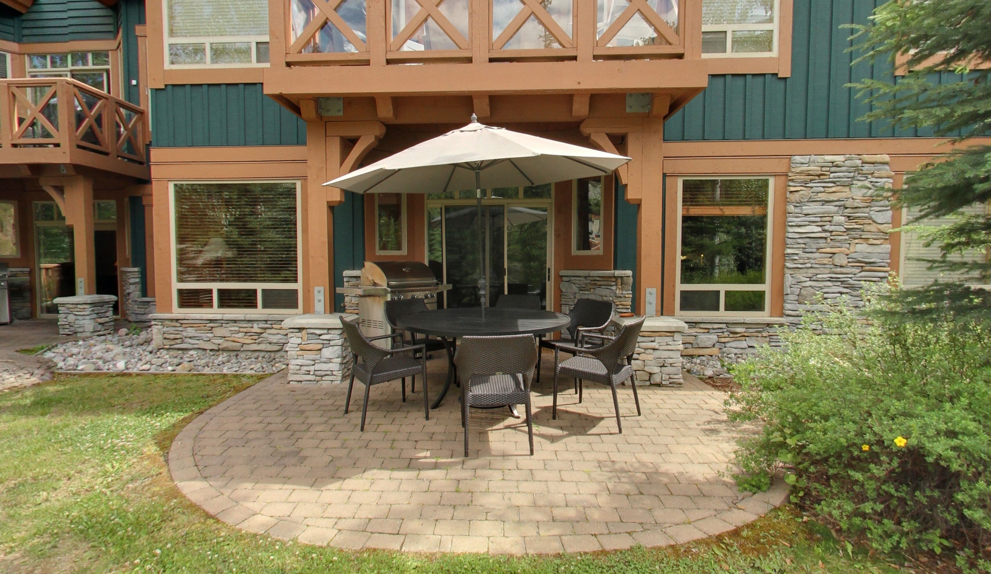 A patio with a round table and chairs, a grill, and a stone wall.