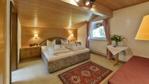 A cozy bedroom with a wooden ceiling, a bed with a floral bedspread, a red rug, and a small table with a lamp. - Gasthof Alpenhof (Mariastein)