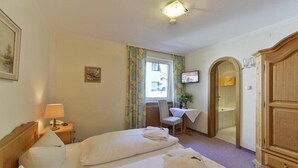 A hotel room with two beds, a desk with a lamp, a television, a wardrobe, and a bathroom with a shower and a bathtub. - Gasthof Alpenhof (Mariastein)