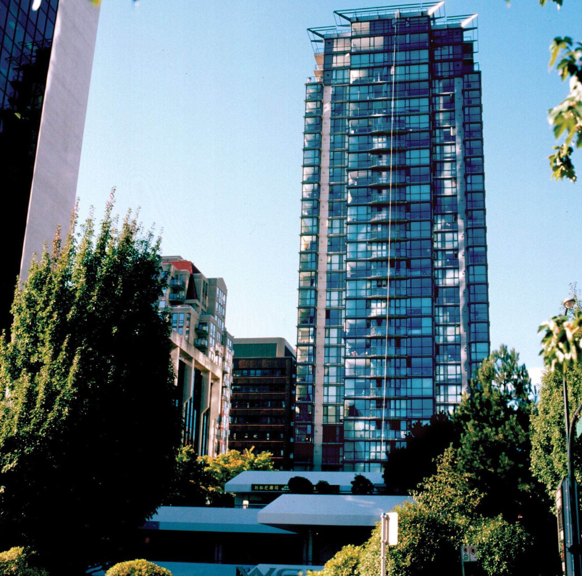 Un edificio moderno de gran altura con fachada de vidrio, rodeado de árboles y otros edificios.