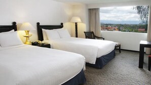 Een hotelkamer met twee bedden, een bureau, een stoel en uitzicht op de stad.