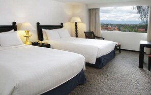 Une chambre d’hôtel avec deux lits, un bureau, une chaise et une vue sur la ville.