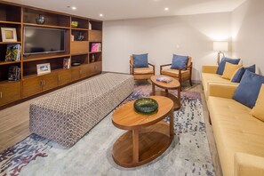 A living room with a sofa, two armchairs, a coffee table, a TV, and a bookshelf. - Marriott Puebla Hotel Meson del Angel (Puebla)