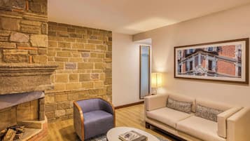 Una sala de estar con chimenea de piedra, un sofá, una silla y un cuadro enmarcado en la pared.