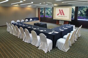 A conference room with a long table, white chairs, and a projection screen displaying the Marriott logo. - Marriott Puebla Hotel Meson del Angel (Puebla)